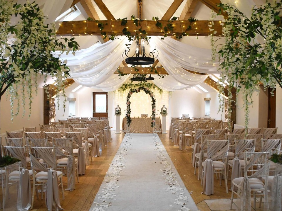 Indoor wedding ceremony room at Beeston Manor, Lancashire, with draped ceiling, fairy lights, aisle runner and floral arch.
