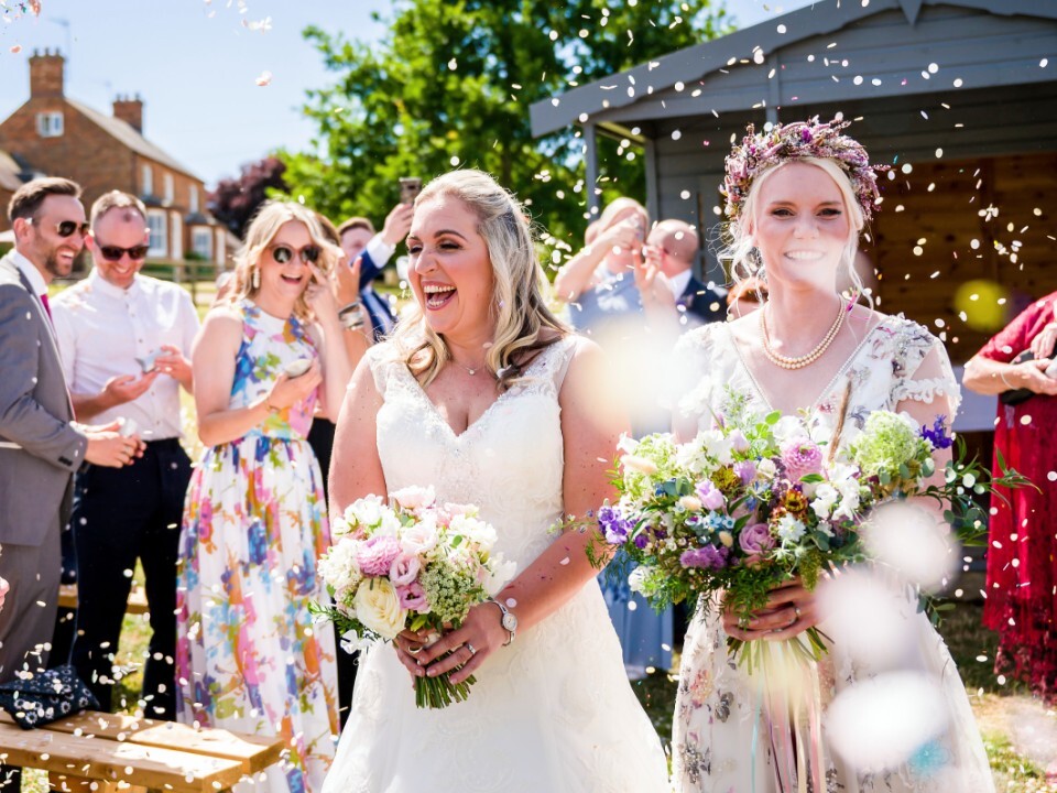 Same-sex couple celebrating their wedding ceremony with guests at a barn wedding venue in the UK