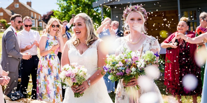 Same-sex couple celebrating their wedding ceremony with guests at a barn wedding venue in the UK