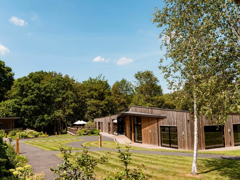The Woodlands at Hothorpe in Leicestershire, featuring contemporary timber lodges, landscaped grounds and woodland surroundings under blue skies.