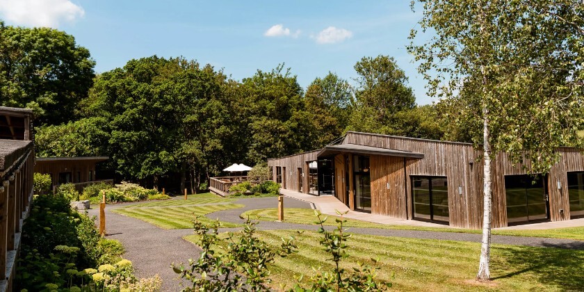 The Woodlands at Hothorpe in Leicestershire, featuring contemporary timber lodges, landscaped grounds and woodland surroundings under blue skies.