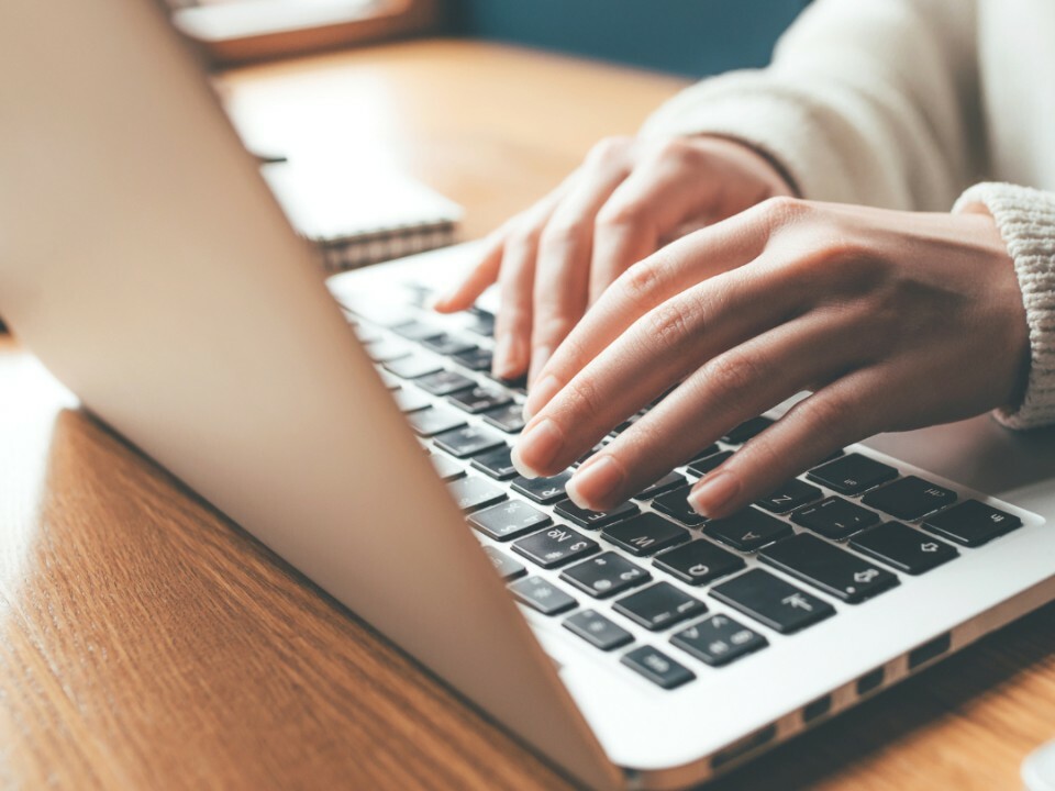 Close-up of a laptop keyboard with a person’s fingers typing on the keys.