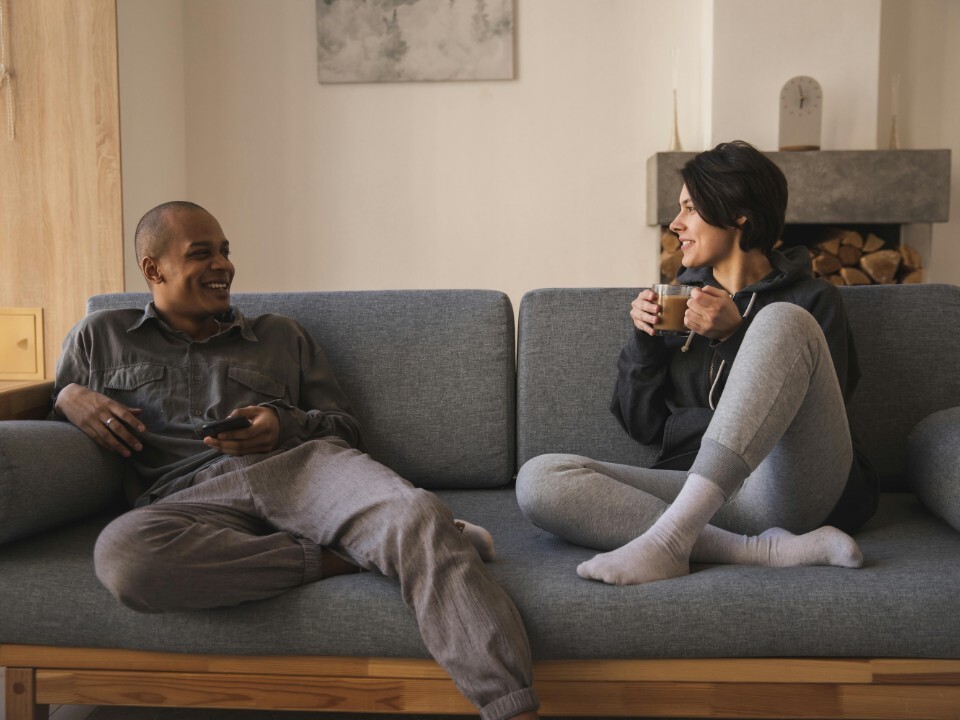 Couple relaxing together at home on the sofa while talking and drinking coffee.