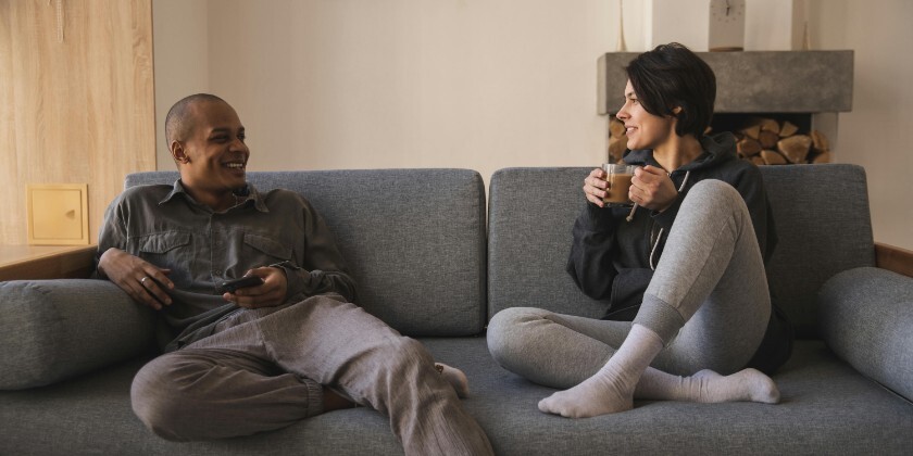 Couple relaxing together at home on the sofa while talking and drinking coffee.