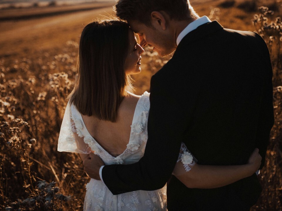 Bride and groom standing in a field at golden hour on their wedding day