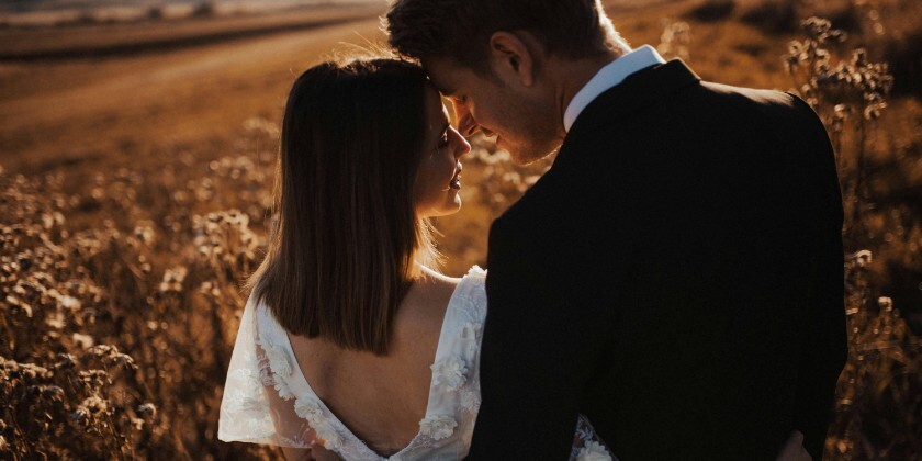 Bride and groom standing in a field at golden hour on their wedding day