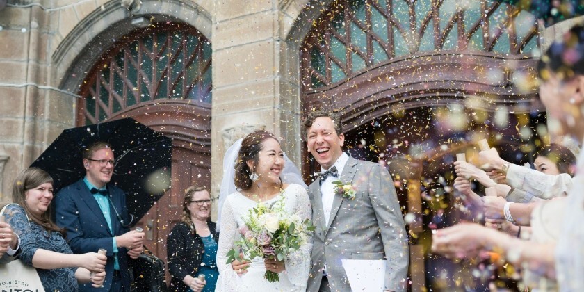 Wedding couple leaving their ceremony as guests throw dried petal confetti, creating a colourful confetti moment outside the venue