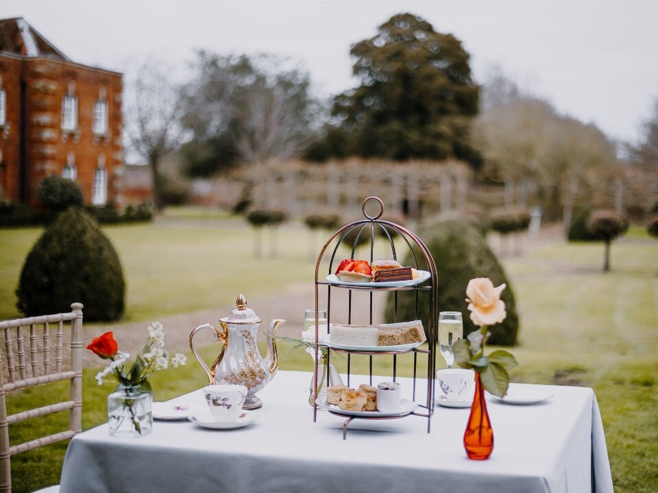 Afternoon tea set up outside in the grounds, with Chicheley Hall wedding venue in the background