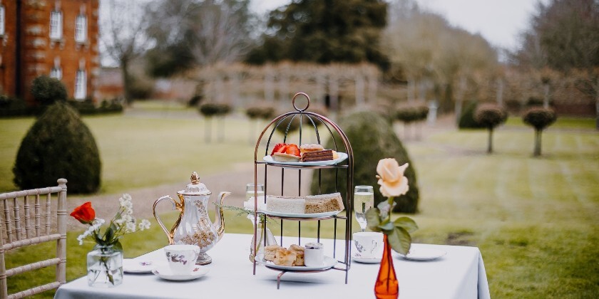 Afternoon tea set up outside in the grounds, with Chicheley Hall wedding venue in the background