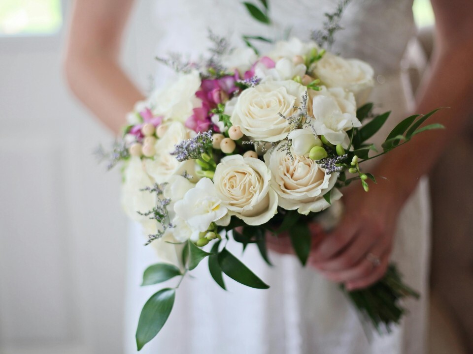 Bride holding a wedding bouquet which prominently features white British roses