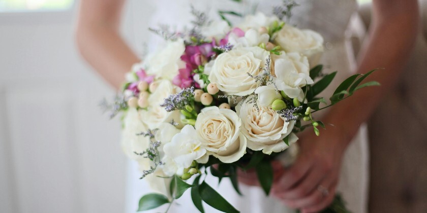 Bride holding a wedding bouquet which prominently features white British roses