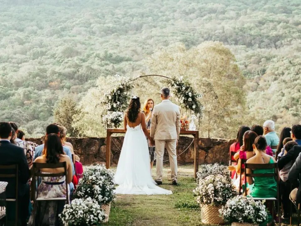 Outdoor wedding ceremony with guests seated on a lawn overlooking a scenic countryside landscape