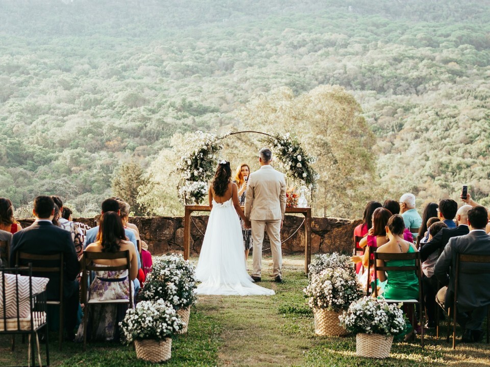 Outdoor wedding ceremony with guests seated on a lawn overlooking a scenic countryside landscape