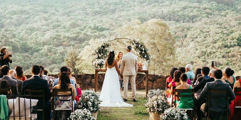 Outdoor wedding ceremony with guests seated on a lawn overlooking a scenic countryside landscape