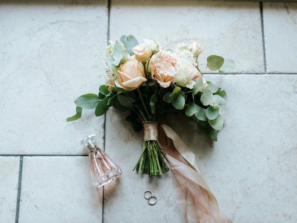 Bridal bouquet made by a wedding florist in a flat lay next to a perfume and wedding rings