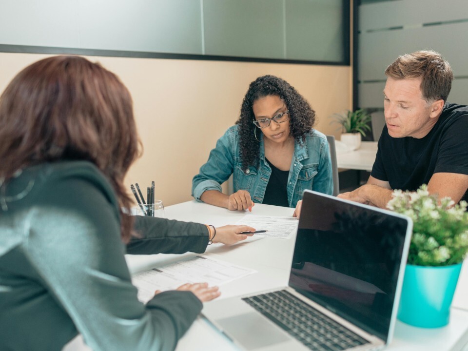 Engaged couple seated at a desk discussing details with another person using a laptop