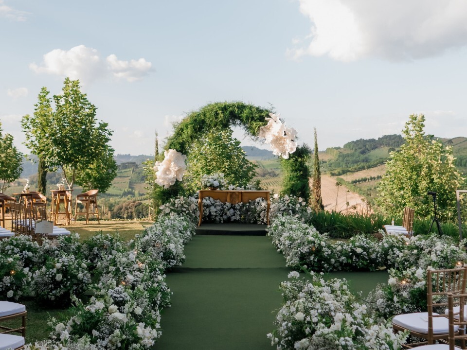 Luxury outdoor wedding ceremony featuring a flower-lined aisle and statement greenery arch overlooking the countryside.