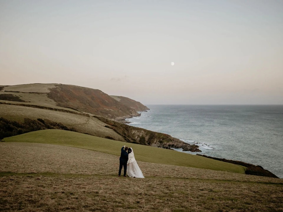 Bride and groom looking at the moon on a cliff in Cornwall by Tredudwell Manor wedding venue