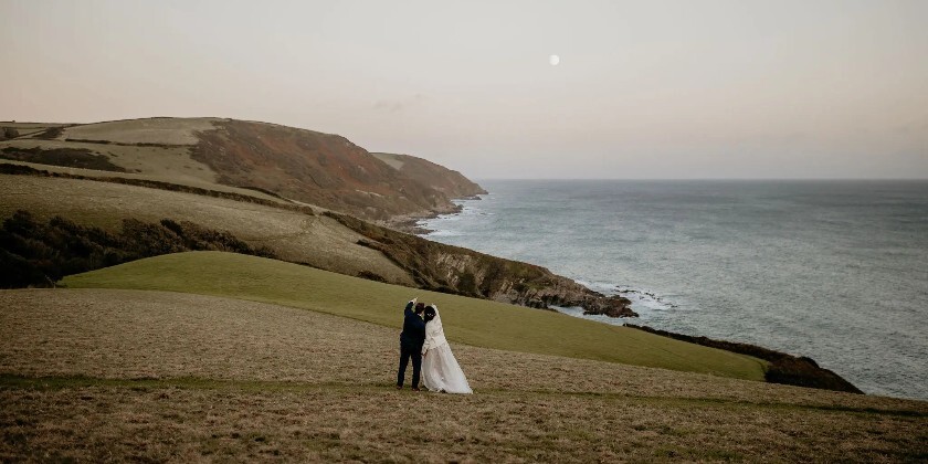 Bride and groom looking at the moon on a cliff in Cornwall by Tredudwell Manor wedding venue