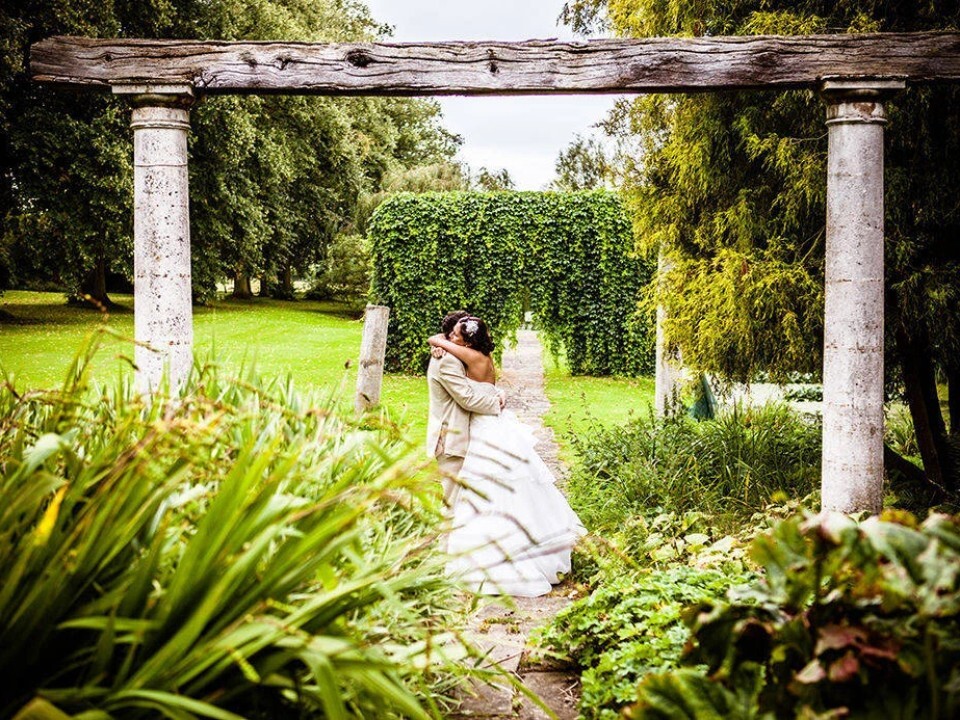 Bride and groom embracing beneath a stone archway in a garden setting, surrounded by greenery at a Leicestershire wedding venue, captured by Lumiere Photography
