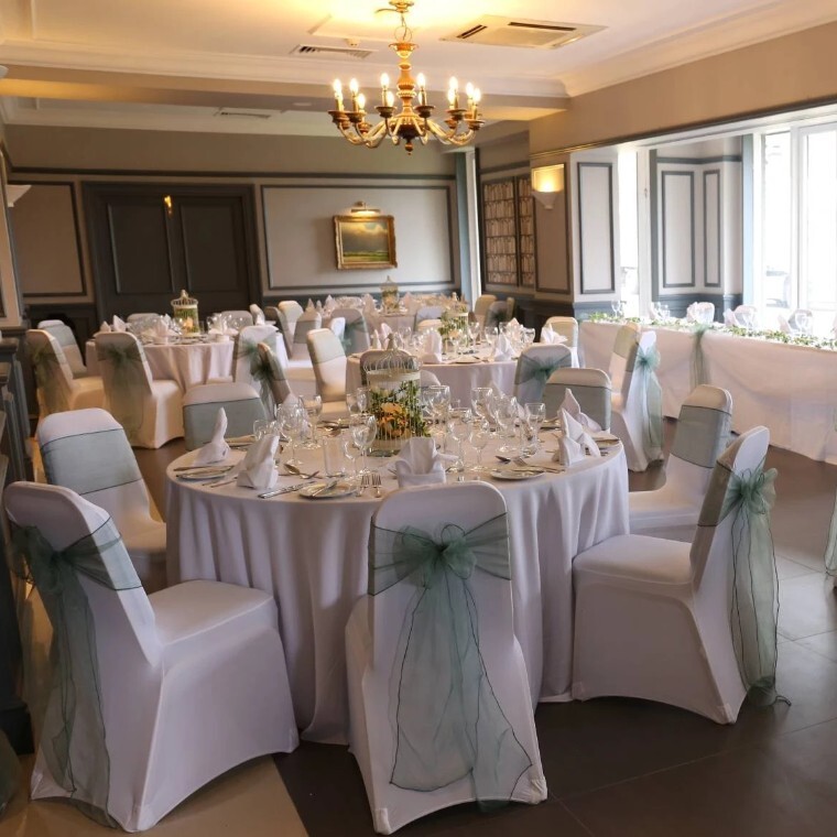 Elegant wedding reception setup at Holiday Inn Maidstone Sevenoaks, with round tables, white linens, chair covers and soft green sashes in a bright function room.