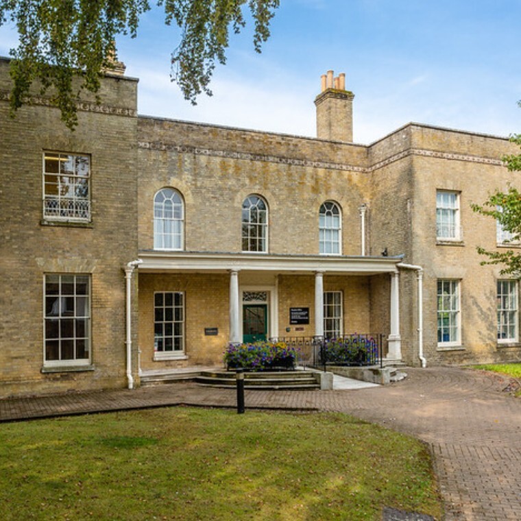 Georgian building with arched windows on the upper, and a covered entryway with pillars. Flower boxes line the pathway leading up to the venue entrance. 