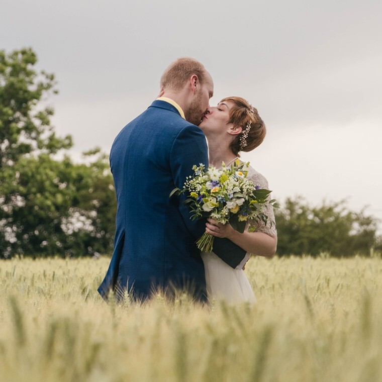 Bride and groom kissing in a field on their wedding day, photographed by EvieSJPhotography.