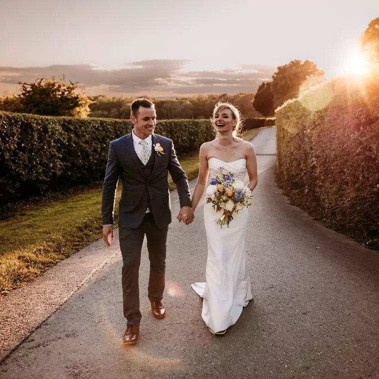 Laughing bride and groom walking holding hands with golden sunset on their wedding day