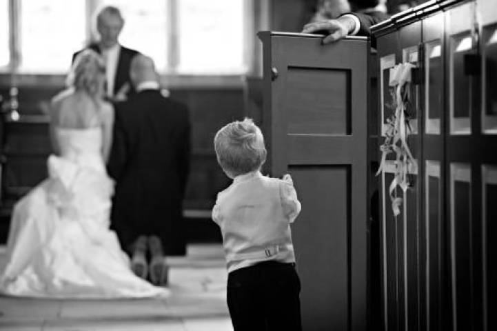 Page boy peaking out of pew at church wedding