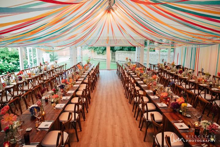 Marquee set for wedding breakfast with colourful streamers draped across the ceiling