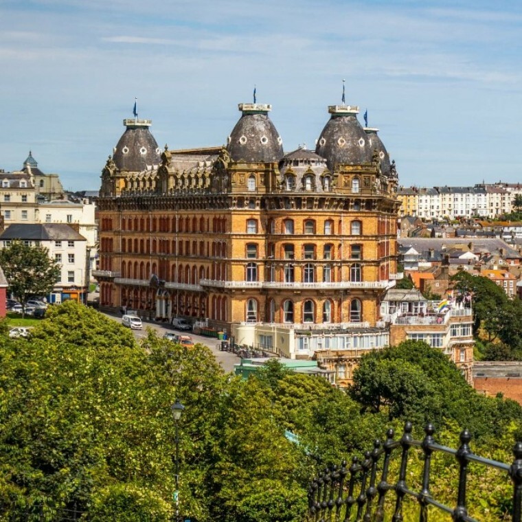 Outside view of the Grand Hotel Scarborough from a distance with greenery and a black metal fence in front of it