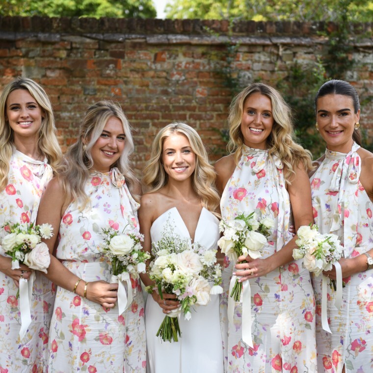 Girls at a wedding in floral dresses holding white floral bouquets in front of a red brick wall
