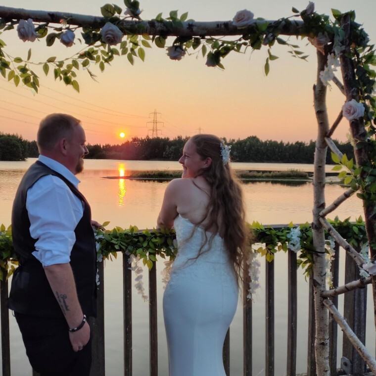 Bride and groom overlooking lake under a wooden arch covered in flowers