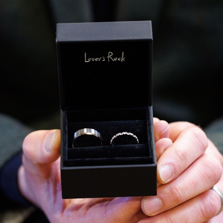 His and Hers Wedding Rings displayed in an open ring box held out with the words "Lovers Rock" on the box 