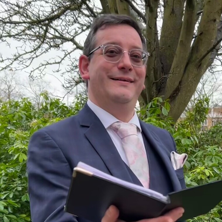 Paul J Abbott of Seratoner Celebrations wearing a smart blue suit and holding custom wedding ceremony script