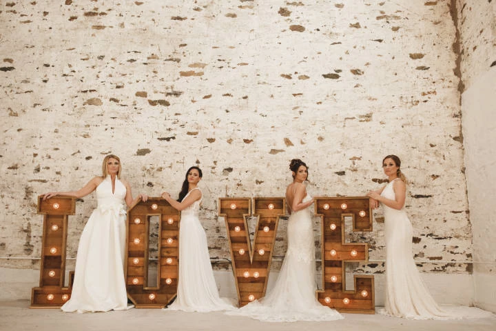 Four brides stood by a large "LOVE" sign