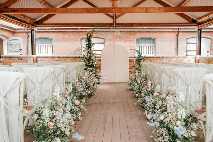 Ceremony set up with chiffon draped chairs and the walkway lined with bright pastel flowers