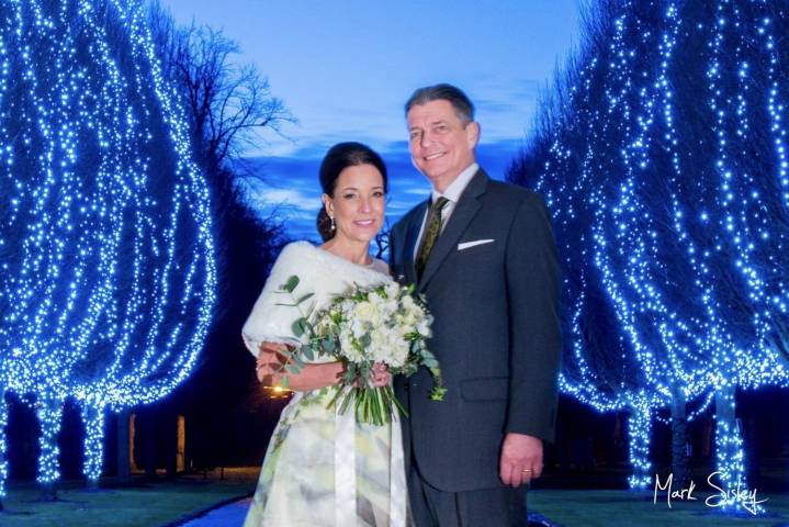 Newlyweds pose for a dusk photo by the avenue of illuminated trees at Danesfield House