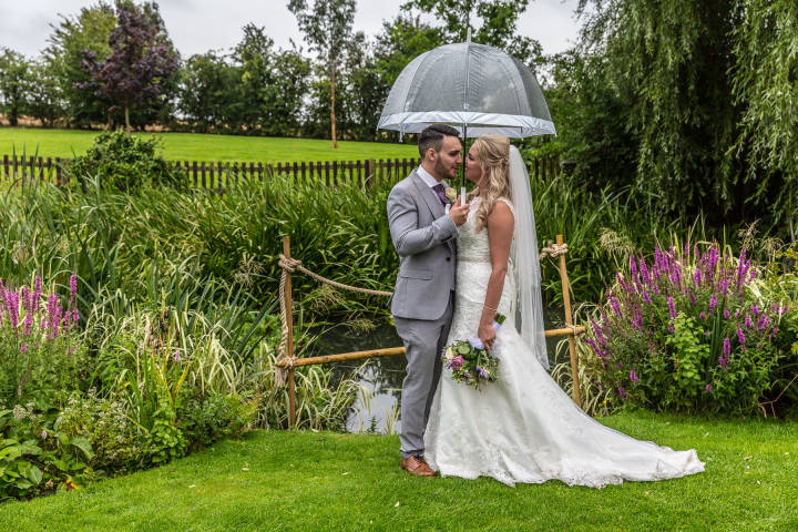 The rain won't stop photos with your loved one. Bride and groom huddled under an umbrella. Wedding p