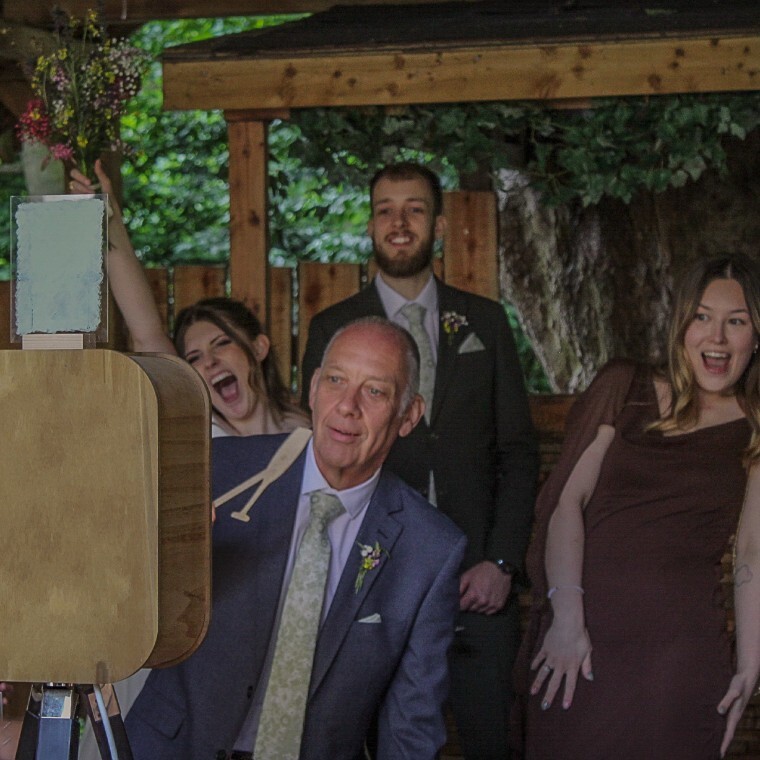 4 wedding guests posing happily in front of a wooden open-air photobooth