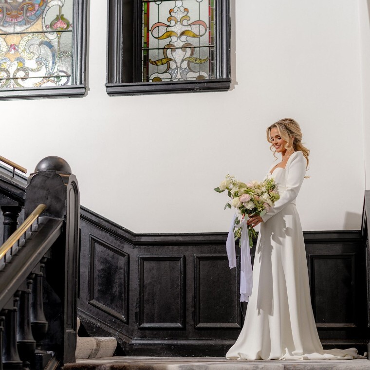 Bride on staircase beneath stained glass windows at The Collector’s Hall wedding venue in Glasgow