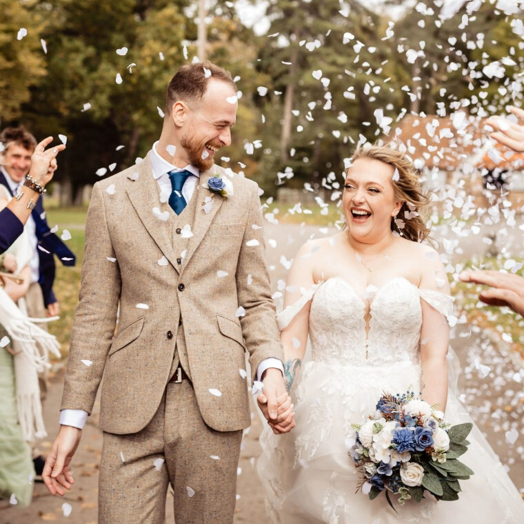 Groom smiles at his bride whilst walking hand in hand through a confett storm