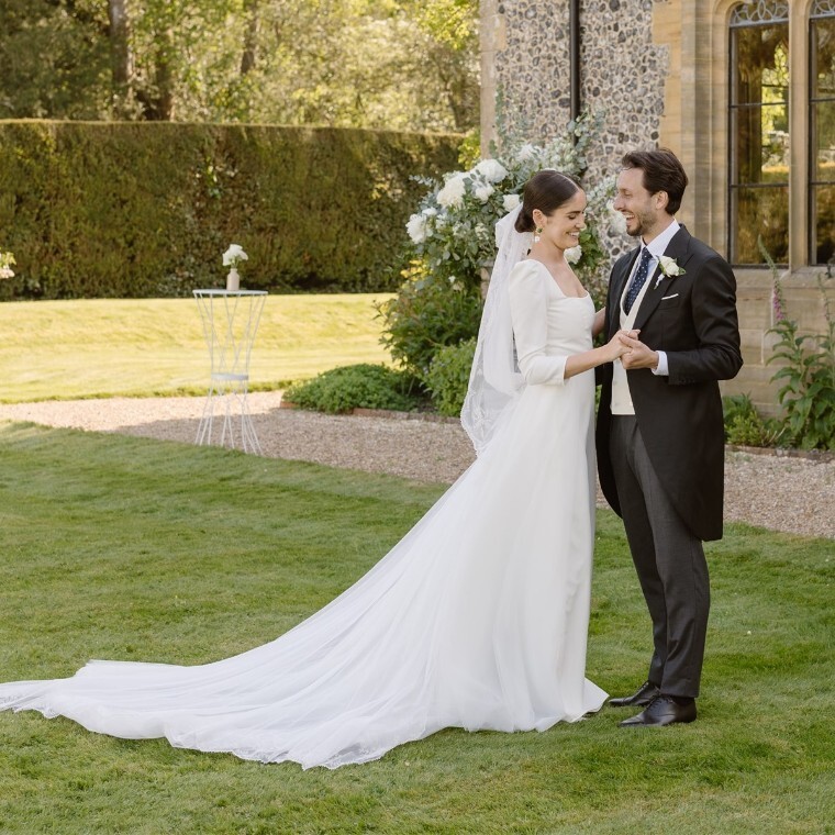 Birde and groom holding hands and smiling on the lawn of a country house