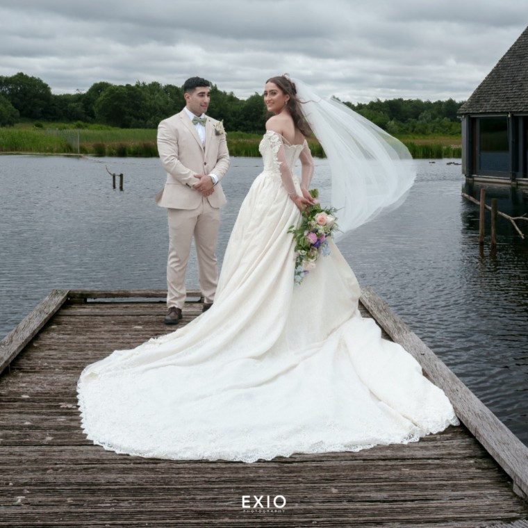 Bride and groom posing for a wedding portrait by the water at Brockholes, captured by Exio Photography