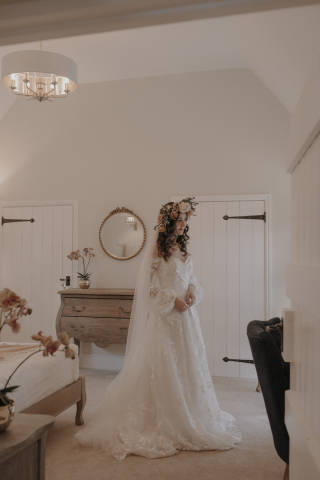 bride with large flower crown standing in a cream bedroom