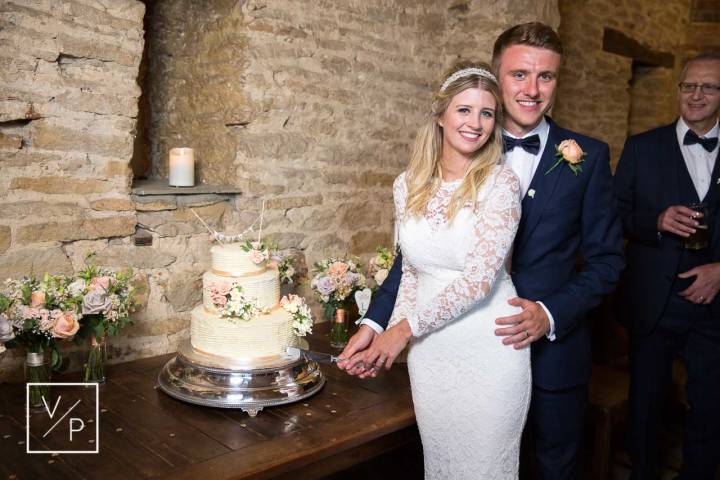 Bride and groom cutting the cake at The Great Barn, Aynho - wedding photography and fun videography 