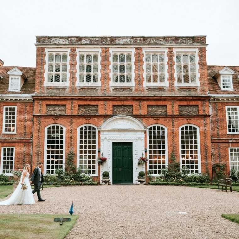 Bride and groom walk beside Gosfield Hall