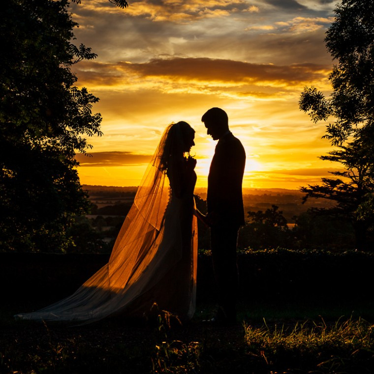bride and groom standing in front of a sunset