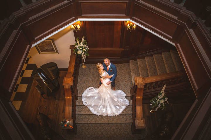 Bride and groom smiling up at the camera stood on a staircase inside Bourton Hall
