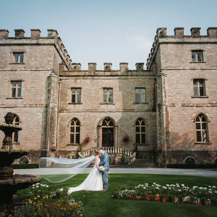 Bride and groom kiss with Clearwell Castle (their wedding venue) as the backdrop